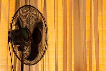 Fan in a warm orange light room cooling a hot summer heat wave. Copy space.