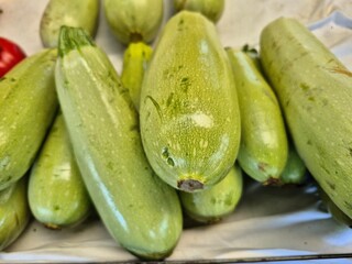Fresh, light green zucchini on display, some rounded, some elongated, showing natural textures and a vibrant, healthy appearance. Ideal for culinary themes.