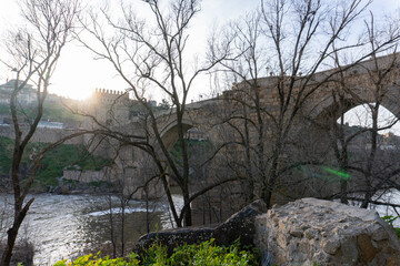 Toledo Old Bridge – The historic San Martín Bridge in Spain gracefully spans the tranquil Tagus River with majestic medieval stone arches and towers, steeped in history and culture