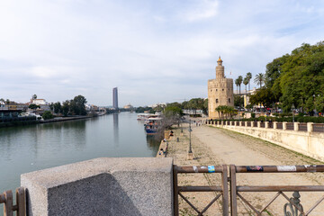 Seville's Serene Vista: A picturesque cityscape of Seville unfurls before the viewer, with the iconic Golden Tower rising majestically beside the tranquil Guadalquivir River.