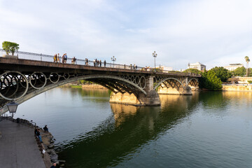 Majestic Bridge over River in the city of Seville Spain: A picturesque arched bridge gracefully spans a tranquil river, with a boat gliding beneath it, offering a serene moment of transportation.r.