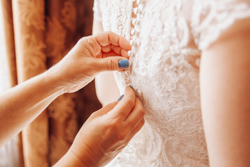 Elegant Female Hands Fastening Buttons on Bride's Back, Intimate Wedding Preparation Moment with Lace Dress Details
