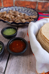 Close-up of a restaurant table with a plate of carnitas, tortillas, and salsas. Mexican food
