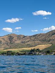 The lush farmland and desolate rolling hills of Chelan country create beautiful contrasts in your view from a boat in Lake Chelan as puffy white clouds dot the sky in summer.
