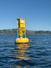 Bright yellow maritime traffic shipping lane marker in puget sound with Tacoma and Mount Rainier in the distance.
