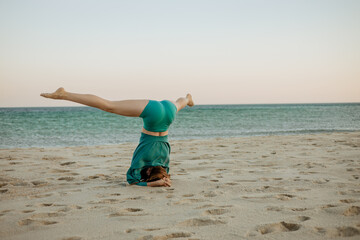 Woman performing Sirsasana (headstand) on the beach during sunrise. Yoga practice by the ocean for strength, balance, and mental focus in a calm, natural environment