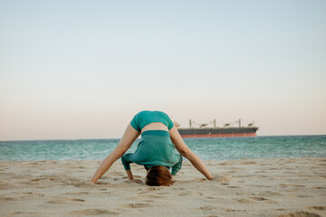 Young woman practicing Prasarita Padottanasana on a sandy beach by the ocean. Morning yoga for flexibility, balance, and inner peace in a serene coastal setting
