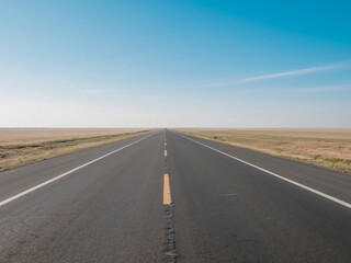 Naklejka premium An empty asphalt road stretching straight into the horizon with a clear blue sky above. Perfect for concepts of travel, freedom, future journey, motivation, adventure, long road trips, and exploring