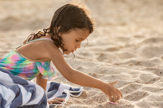 Little child girl playing with sand at the beach at summer sunset in Florida