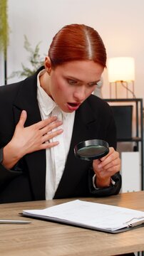 Young businesswoman at home office inspects contract through magnifying glass spots commission and scowls. Freelancer girl at table confronts fee clause demanding change angered by unfair extra cost