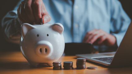 Businessman saving money with white piggy bank and stacked coins on wooden table, concept for financial planning, investment, and budget management in modern business and personal finance.
