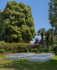 White chairs lined up before wedding ceremony in a public park with lush greenery around the venue.