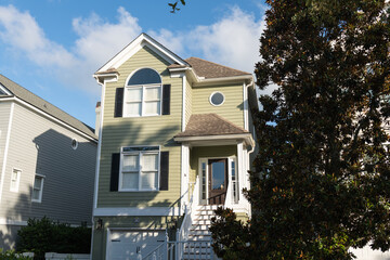 Isle of Palms, South Carolina, USA - June 30, 2025: A light green two-story coastal home with black shutters and distinctive arched and circular windows, under clear summer skies at Wild Dunes Resort