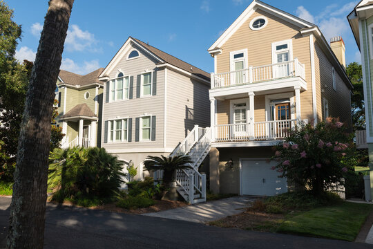 Isle of Palms, South Carolina, USA - June 30, 2025: A row of pastel-colored coastal homes with balconies and palm trees along a quiet residential street under a sunny blue sky. - Powered by Adobe