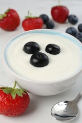 Tasty yoghurt with blueberries and strawberries in bowl on white table, closeup