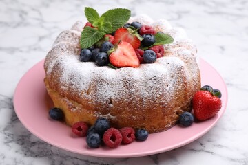 Tasty Bundt cake with powdered sugar and berries on white marble table, closeup