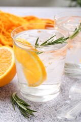 Sparkling water with orange slices and rosemary on grey table, closeup
