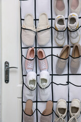 Organizer with different footwear on door indoors. Shoe storage