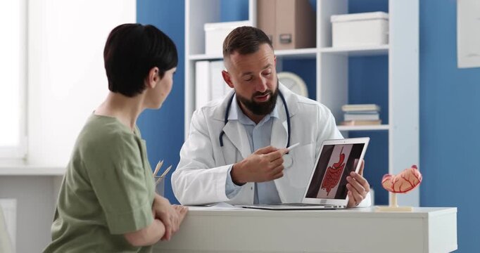 Gastroenterologist showing screen with illustration of large intestine to patient in clinic, camera moving left