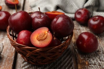 Ripe cherry plums and wicker basket on color wooden table, closeup