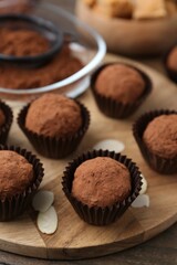 Delicious homemade candies powdered with cocoa on wooden table, closeup