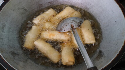 Several rissoles being deep-fried in a large metal wok with hot oil, showing traditional cooking and street food preparation.
