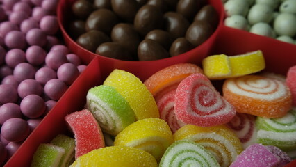 A vibrant candy tray filled with chocolate-covered treats, jelly candies, sugar-coated sweets, and colorful round candies in sections.
