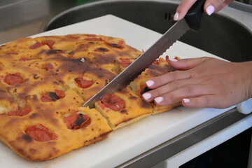 mani tagliano una focaccia fatta in casa con un grande coltello