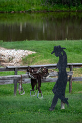 Cowboy Silhouette with Saddle on Wooden Fence by Pond
