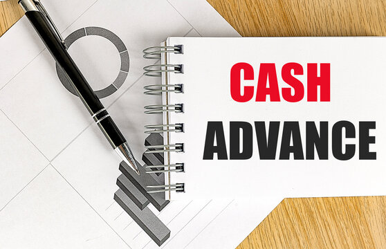 Cash advance text on notepad with pen and financial chart on wooden desk