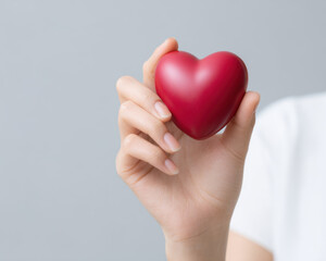 Fototapeta premium Close up of hand gently holding smooth red heart shape, symbolizing love and care with soft gray background