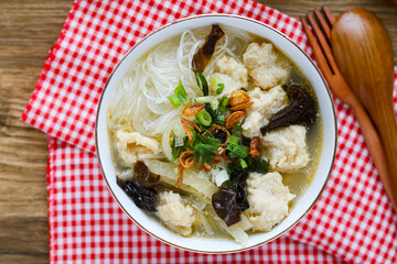 Top view of a comforting bowl of traditional Indonesian Tekwan, a flavorful fish cake soup with glass noodles, mushrooms, and fresh herbs, served in a white bowl.