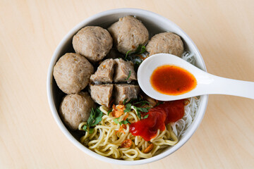 Top view of Bakso (or Baso), a popular meatball soup. The broth is filled with beef meatballs, yellow noodles, vermicelli, garnished with fried shallots, chopped greens and a spoon of chili.