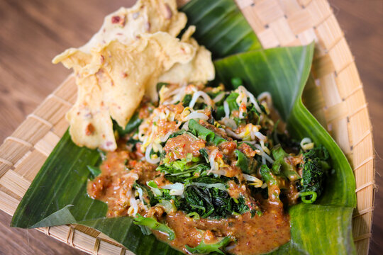 Closeup of Pecel, a traditional Indonesian salad featuring blanched vegetables, bean sprouts, and long beans, drizzled with a peanut sauce. Served on a banana leaf with crispy rempeyek crackers.