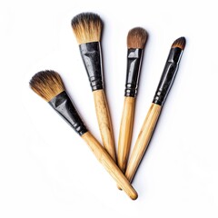 Four makeup brushes, light brown wooden handles, black tips, and fluffy, light brown heads, arranged fan-like against a white background