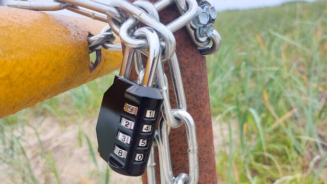 Close-up of combination padlock fastening metal chain around yellow metal barrier, emphasizing security and restricted access