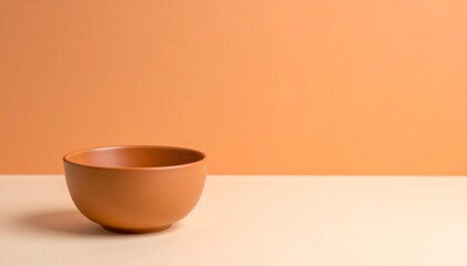 小さなテラコッタボウルが、暖かいオレンジからクリームに変化するマットグラデーション背景の左下に配置されています。