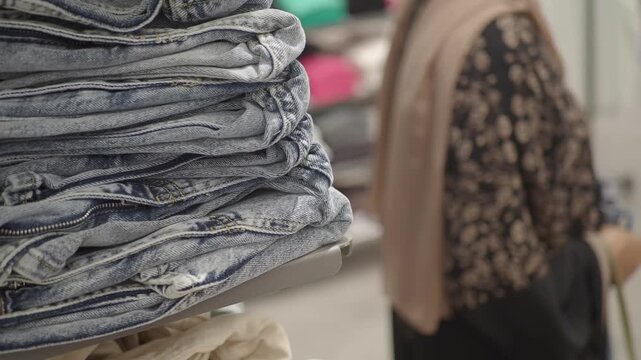 stack of folded jeans in a clothing store with a person browsing