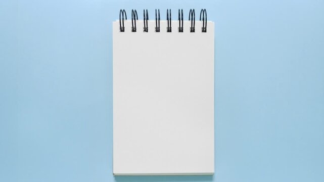 Stop motion of a blank spiral sketchbook sliding onto a blue backdrop, ideal for copy space