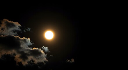 A luminous full moon shines brightly through dark, fluffy clouds in the night sky.