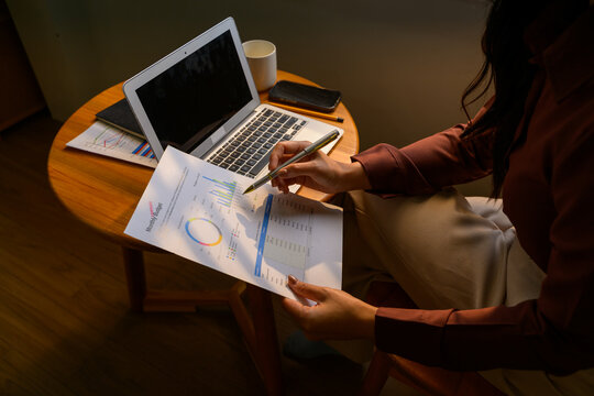 Businesswoman analyzing financial report using laptop at home office desk