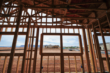Obraz premium Wood framing of a residential home under construction shows interior wall studs, window openings, and roof trusses, with additional new houses visible across the future subdivision development site