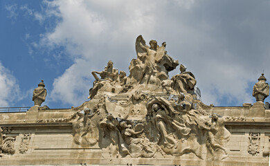 sculptural group adorning the pediment of a theater building, featuring dynamic figures in flowing robes and dramatic poses. The stone relief showcases classical mythology in Lille, France.