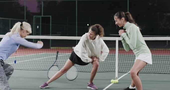Coach doing lunges in activewear at dusk tennis court Diverse female friends following with rackets