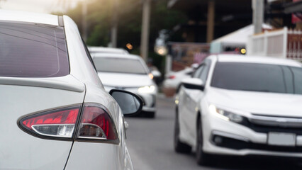 Rear side of white car driving on the asphalt road. Other cars driving past from the opposite side. Background of city under view of dark trees with light.
