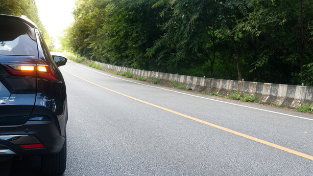 Rear side of dark blue car with turn light signal. Stop or travle to nature on asphalt road up to hills. Beside with green forests under bight sky.