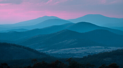 Naklejka premium A scenic view of layered blue mountains under a pink and purple colored sky at dusk