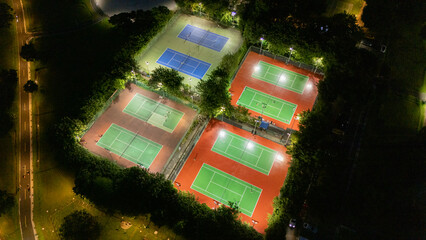 Nighttime Aerial View of Illuminated Tennis Courts Lush Green Surroundings