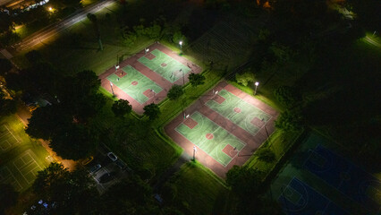 Aerial View of Illuminated Tennis Courts in Lush Greenery at Night