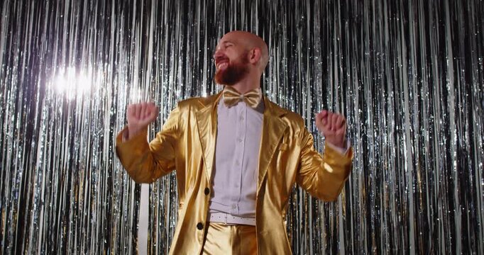 Happy man in a gold suit dancing to music during a disco party on a shiny background. Evening celebration features fun, entertainment, and vibrant nightlife, creating a lively and festive atmosphere.